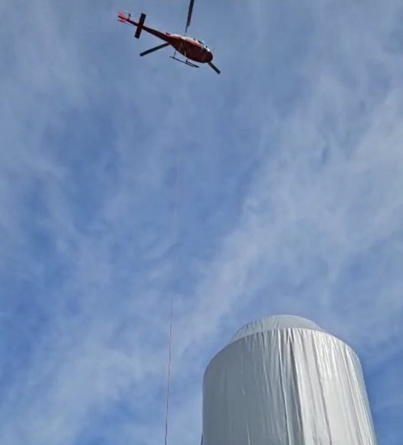 Ein Helikopter schwebt über dem verhüllten Weissen Turm von Mulegns kurz vor der feierlichen Enthüllung.