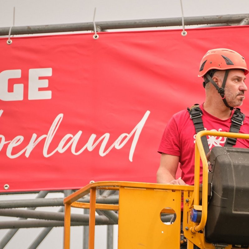 Monteur befestigt auf einer Hebebühne eine ESAF-2025-Blache an der Tribünenkonstruktion.