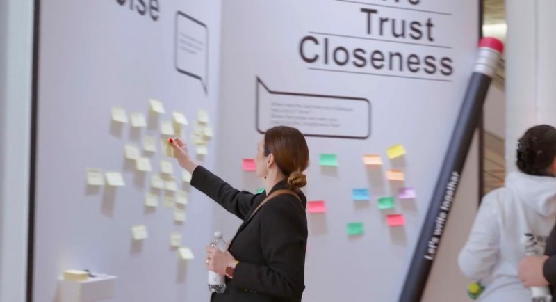 Eine Mitarbeitende klebt Post-it Zettel ins überdimensionale Buch 