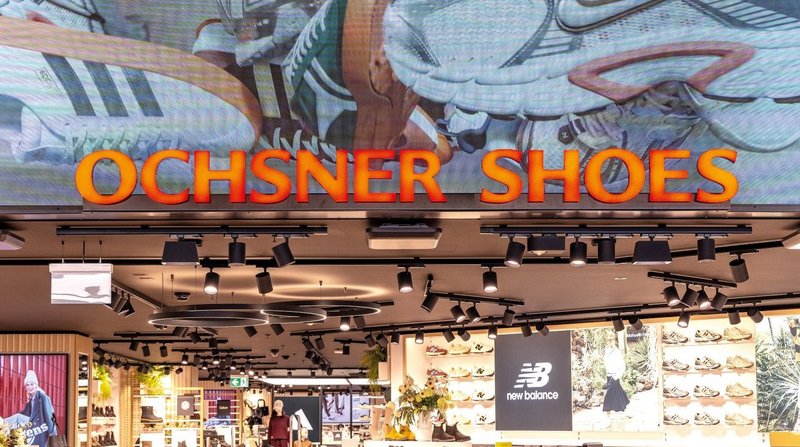 LED-Display mit 3D-Visualisierung und auffälligem Neon-Schriftzug am Eingang von Ochsner Shoes im Einkaufszentrum Tivoli.