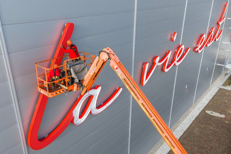 Installers from Richnerstutz on an aerial work platform assembling illuminated letter segments of the facade signage for Bell Switzerland.