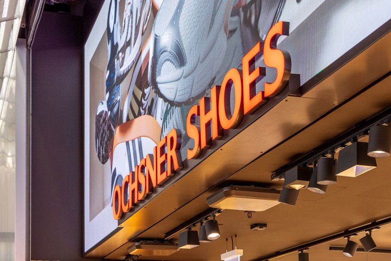 3D-fähiger LED-Screen des Typs Uslim II mit hellem Schriftzug – installiert über dem Eingang von Ochsner Shoes im Tivoli Spreitenbach