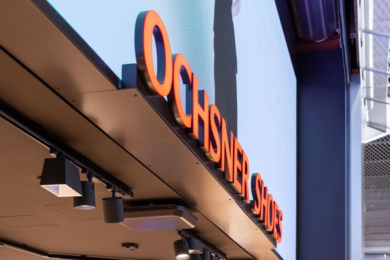 Moderner LED-Screen mit 3D-Tiefeneffekt und beleuchtetem Schriftzug, angebracht über dem Haupteingang von Ochsner Shoes im Tivoli.
