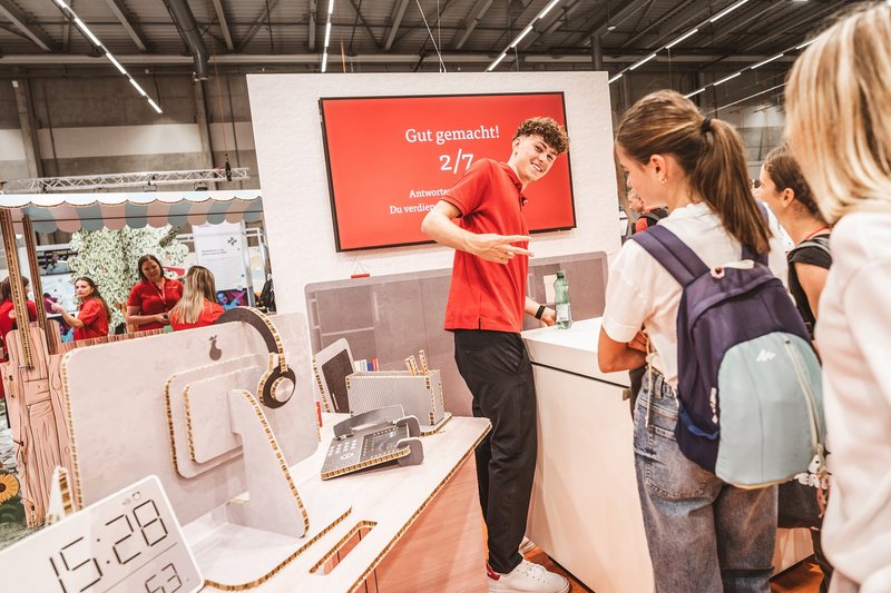 SwissSkills Messestand aus Wabenkarton und interessierte Besucherinnen. Die Mobiliar hat 300 m2 Messestand aus diesem Material gefertigt. Bis auf ein paar Ausnahmen wie Screens sind alle Elemente und Accessoires aus Karton: Stellwand, Tisch, Stuhl, Laptop usw.