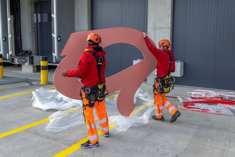 Installers from Richnerstutz lifting an illuminated letter segment of the facade signage for Bell Switzerland.