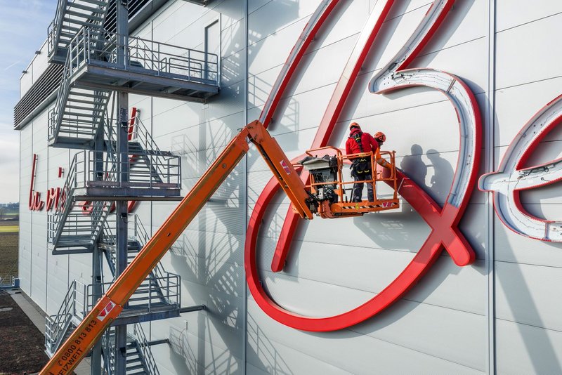 Drone shot of installers from Richnerstutz on an aerial work platform assembling illuminated letter segments of the facade signage for Bell Switzerland.