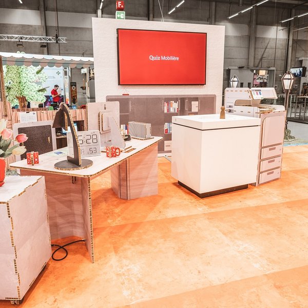 SwissSkills Messestand aus Wabenkarton. Die Mobiliar hat 300 m2 Messestand aus diesem Mobiliar gefertigt. Bis auf ein paar Ausnahmen wie Screens sind alle Elemente und Accessoires aus Karton, wie: Blumenstrauss, Tischlampe, Schreibtisch, Uhr, Kommode, Stellwand mit integriertem Screen, Verkaufsstand usw.