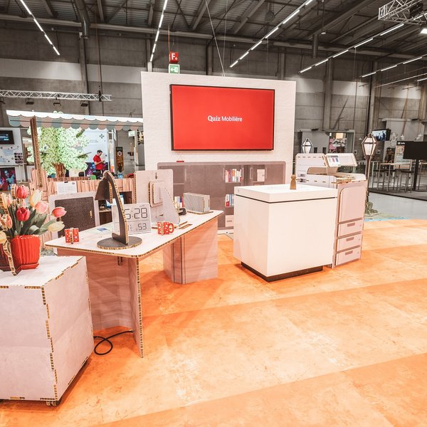 SwissSkills Messestand aus Wabenkarton. Die Mobiliar hat 300 m2 Messestand aus diesem Mobiliar gefertigt. Bis auf ein paar Ausnahmen wie Screens sind alle Elemente und Accessoires aus Karton. wie: Blumenstrauss, Tischlampe, Schreibtisch, Uhr, Kommode, Stellwand mit integriertem Screen, Verkaufsstand usw.
