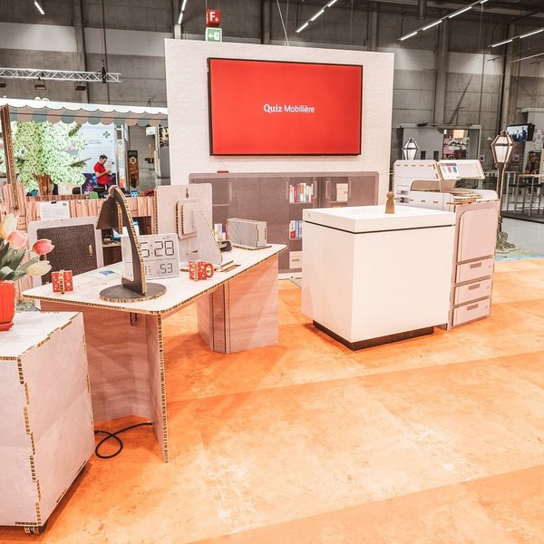 SwissSkills exhibition stand made from honeycomb cardboard. Die Mobiliar created a 300 m² exhibition stand from this material. Except for a few items such as screens, all elements and accessories are made of cardboard, including: bouquet, table lamp, desk, clock, chest of drawers, partition wall with integrated screen, sales counter, etc.