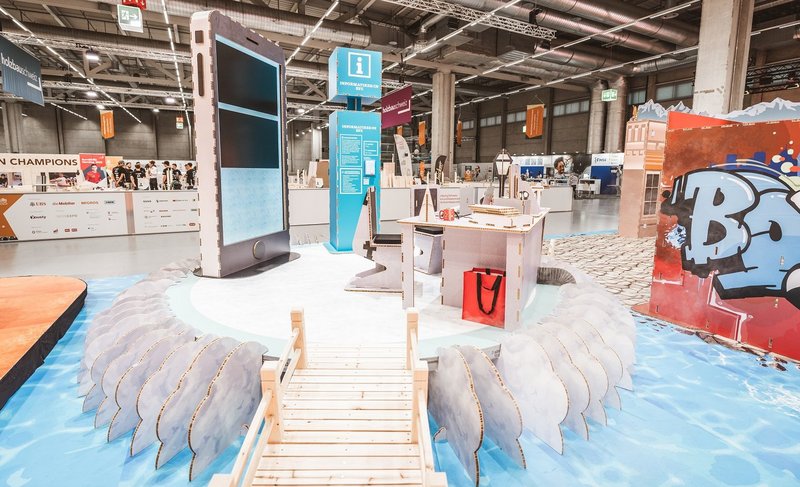 SwissSkills Messestand aus Wabenkarton. Die Mobiliar hat 300 m2 Messestand aus diesem Material gefertigt. Bis auf ein paar Ausnahmen wie Screens sind alle Elemente und Accessoires aus Karton. Eisscholle mit riesigem Mobile, Info-Point, Pult, Stuhl und Side board aus Wabenkarton
