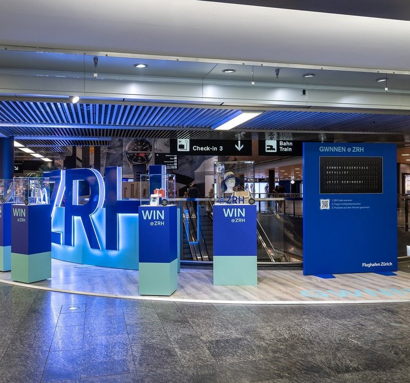 Begehbare Promotion am Flughafen Zürich mit Acrylglas-Buchstaben und Vitrinen, gestaltet als interaktive Erlebniswelt.