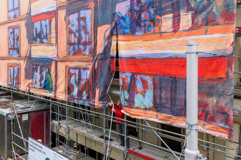 Montage einer Baugerüstbespannung mit originalgetreuem Grossformatdruck: Ein Monteur richtet eine bedruckte Gitternetz-Blache am Baugerüst aus und befestigt sie als Gerüstverkleidung; die Grossformat-Reproduktion basiert auf einem Acrylgemälde von Michele Bordoni und wurde von Richnerstutz als Blachen-Druck/Grossformat umgesetzt.