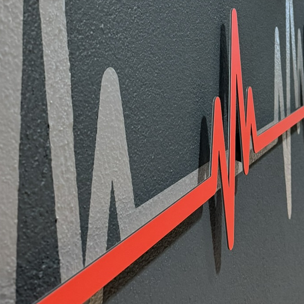 Rote Herzschlag-Kurve aus Dibond mit 3D-Abstandshaltern vor grauer Folie an einer Wand.