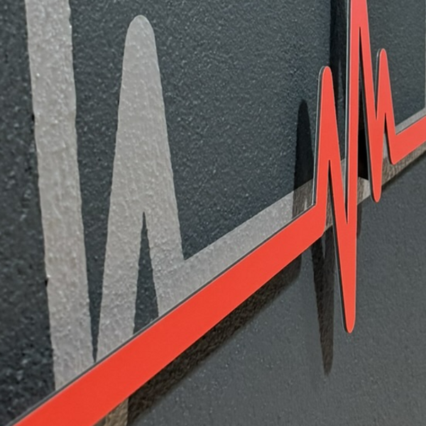 Rote Herzschlag-Kurve aus Dibond mit 3D-Abstandshaltern vor grauer Folie an einer Wand.