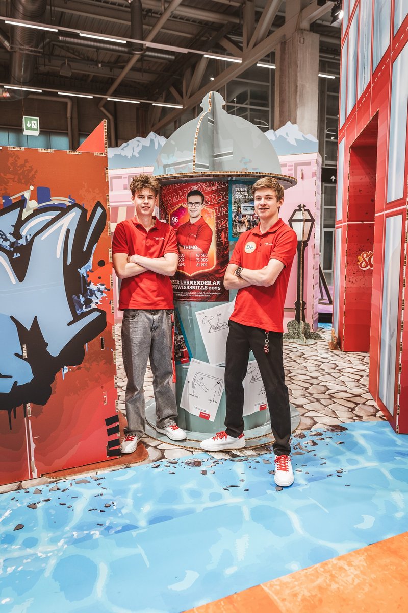 SwissSkills Messestand aus Wabenkarton. Die Mobiliar hat 300 m2 Messestand aus diesem Material gefertigt. Bis auf ein paar Ausnahmen wie Screens sind alle Elemente und Accessoires aus Karton.Ein Duo von die Mobiliar steht vor einer Litfasssäule bereit, um die jungen Messebesuher zu empfangen.
